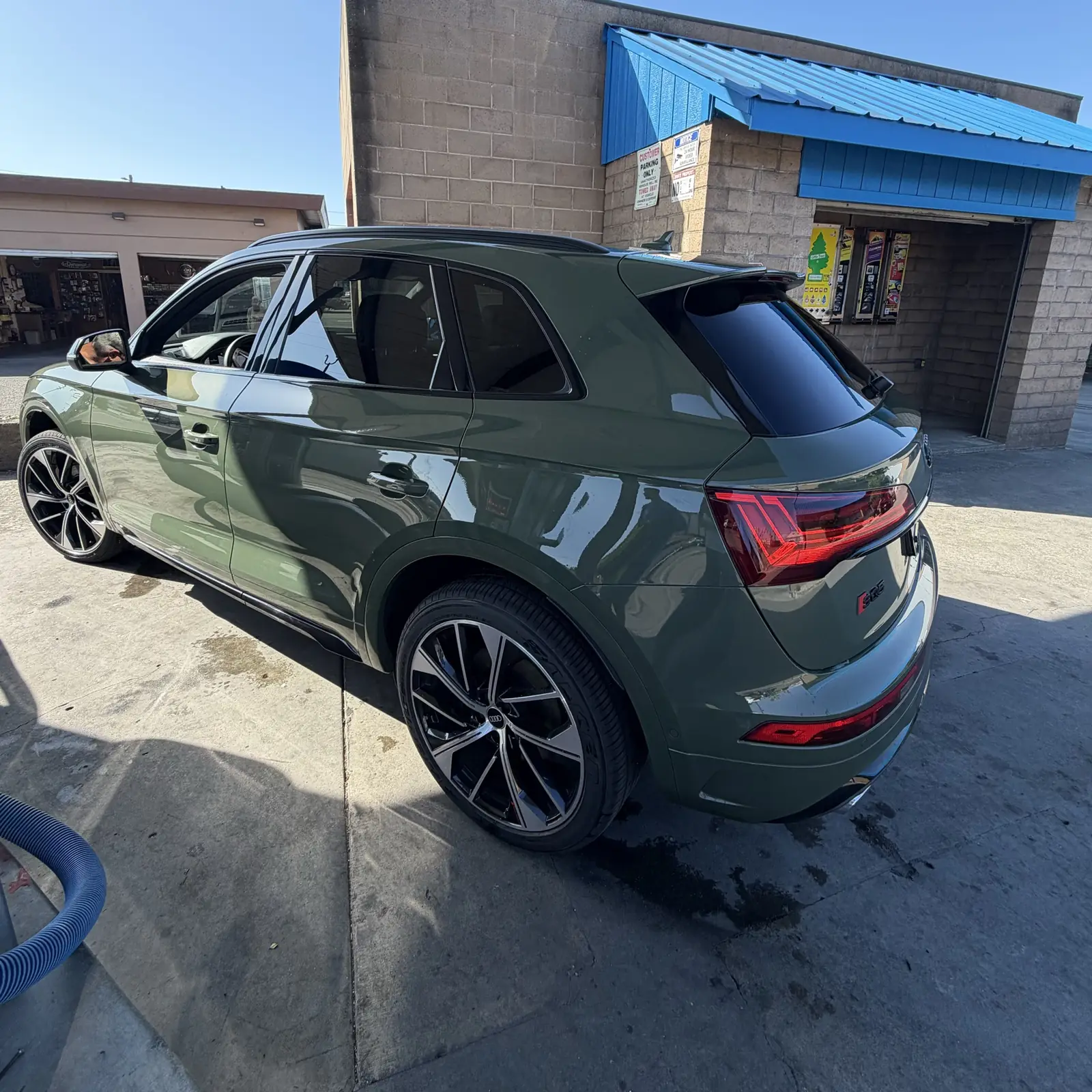 A green Audi SUV, washed and dried, beside the blue-roofed bays