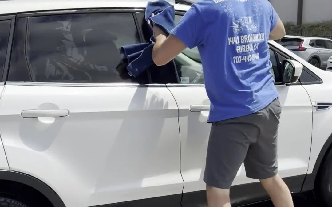 A Zenith crew member hand drying a white SUV with a towel after the tunnel