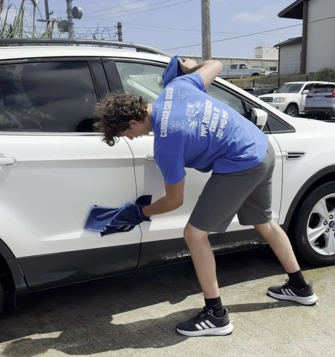 A crew member hand drying the door of a white SUV with a towel after the tunnel